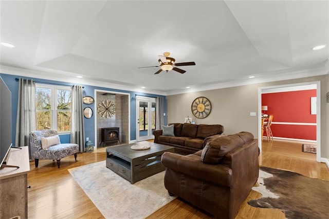 living room featuring light wood-style floors, a tray ceiling, a tile fireplace, and recessed lighting