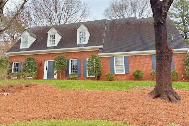 new england style home with brick siding, a front lawn, and a shingled roof