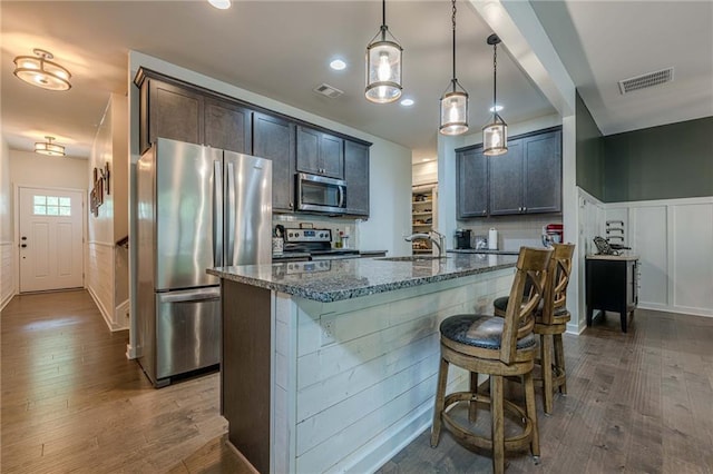 3291 Wild Basil Ln, Buford, GA 30519 - kitchen with appliances with stainless steel finishes, dark stone countertops, dark wood-type flooring, an island with sink, and a breakfast bar area