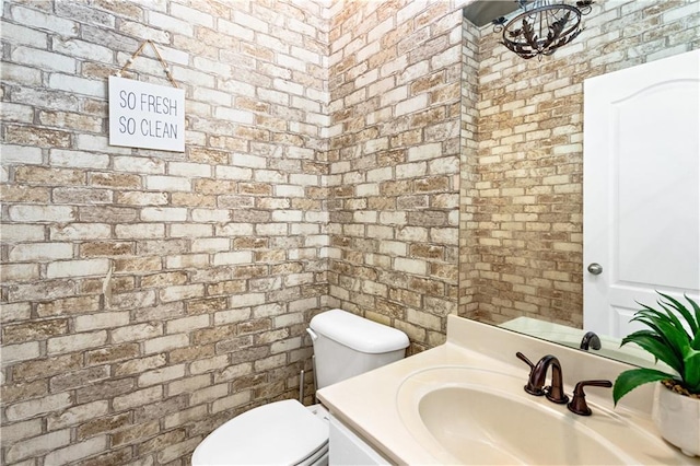 bathroom featuring vanity, brick wall, and toilet