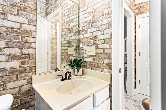 bathroom with brick wall, toilet, and vanity