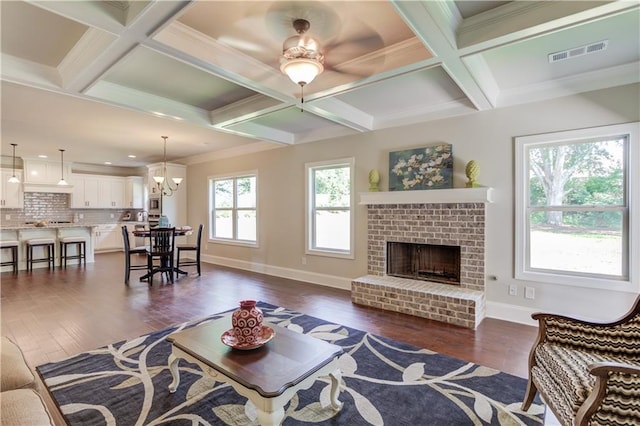 living room featuring beam ceiling, dark hardwood / wood-style floors, coffered ceiling, ornamental molding, and a brick fireplace