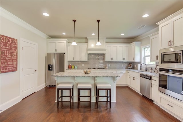 kitchen with pendant lighting, stainless steel appliances, a kitchen island, and white cabinets