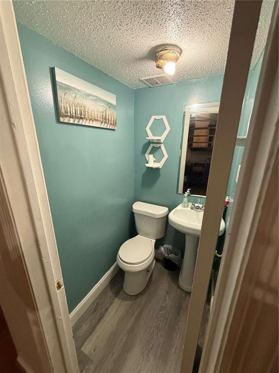 bathroom featuring wood-type flooring, toilet, sink, and a textured ceiling