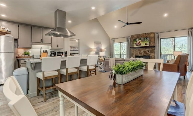 dining space with ceiling fan, plenty of natural light, a stone fireplace, and light hardwood / wood-style floors