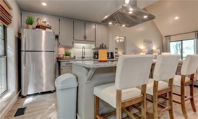 kitchen featuring a kitchen island, island range hood, gray cabinetry, stainless steel fridge, and light stone countertops