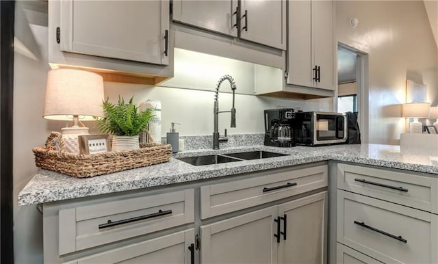 kitchen featuring light stone counters, sink, and white cabinets