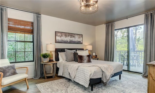 bedroom with wood-type flooring, access to exterior, and an inviting chandelier