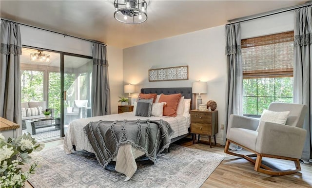 bedroom with an inviting chandelier, access to outside, and light wood-type flooring