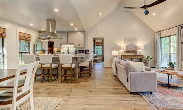 living room featuring ceiling fan, a wealth of natural light, high vaulted ceiling, and light hardwood / wood-style flooring