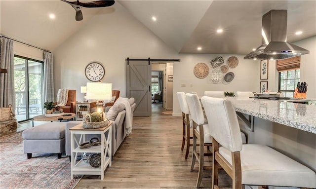 living room featuring ceiling fan, a barn door, high vaulted ceiling, and light hardwood / wood-style flooring