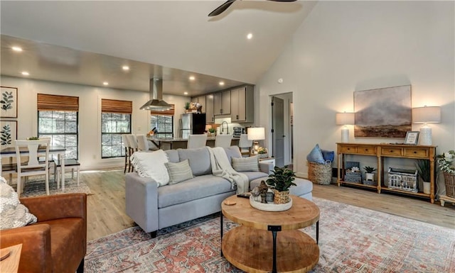 living room with high vaulted ceiling, ceiling fan, and light hardwood / wood-style flooring