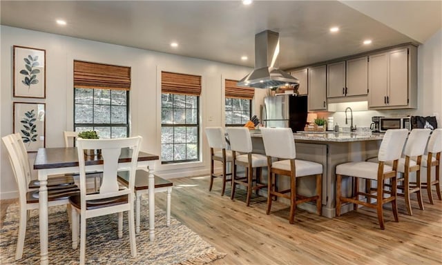 kitchen with stainless steel fridge, light hardwood / wood-style flooring, gray cabinetry, light stone counters, and island range hood