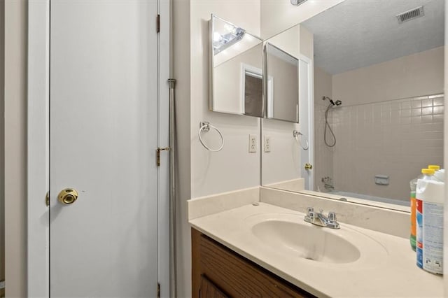 bathroom with vanity, a textured ceiling, and tiled shower / bath