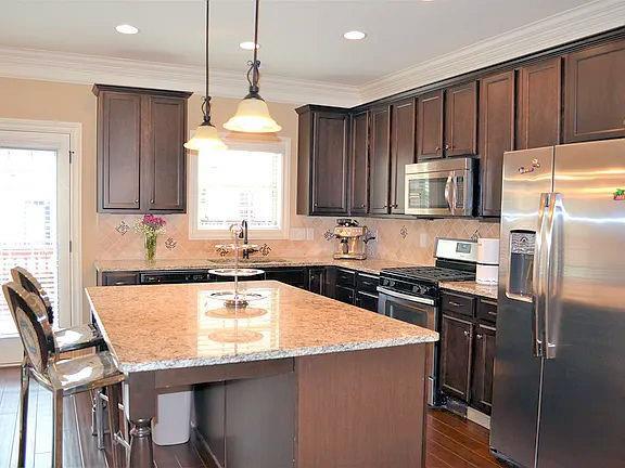 1035 Willow Field Ln SE, Marietta, GA 30067 - kitchen with light stone counters, dark brown cabinets, a kitchen island, appliances with stainless steel finishes, and dark wood-style flooring