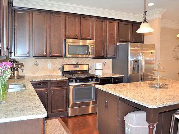 1035 Willow Field Ln SE, Marietta, GA 30067 - kitchen featuring backsplash, dark brown cabinets, decorative light fixtures, light stone countertops, and appliances with stainless steel finishes