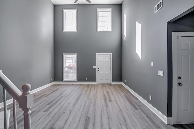 foyer with ceiling fan, light hardwood / wood-style floors, and a towering ceiling