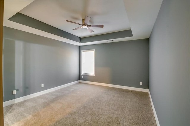 empty room with a tray ceiling, ceiling fan, and carpet floors