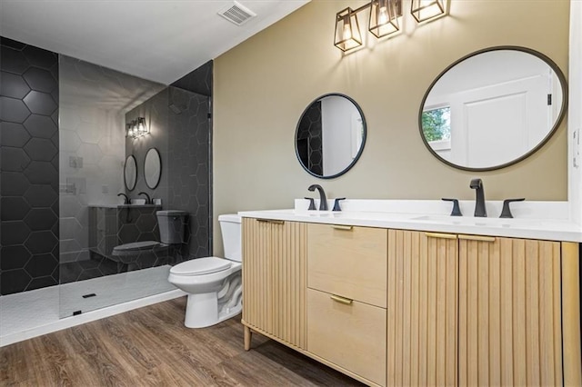 bathroom with double vanity, visible vents, toilet, a sink, and wood finished floors