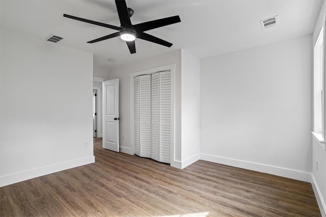 unfurnished bedroom with a closet, visible vents, baseboards, and wood finished floors