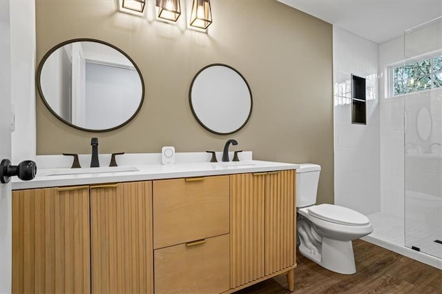 full bathroom with double vanity, toilet, wood finished floors, a tile shower, and a sink