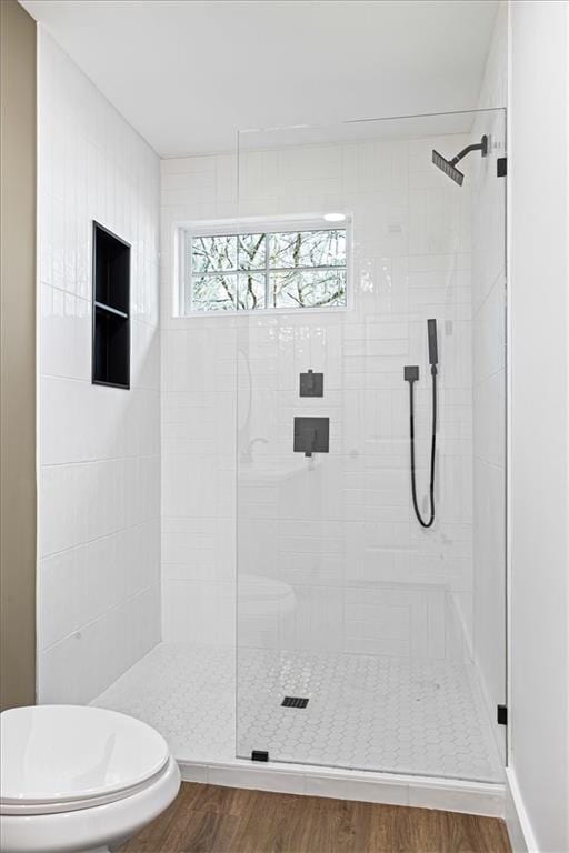 bathroom with tiled shower, toilet, and wood finished floors