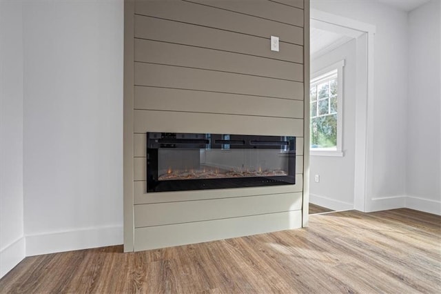 room details featuring baseboards, wood finished floors, and a glass covered fireplace