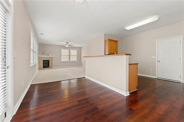 unfurnished living room with dark hardwood / wood-style flooring, a tile fireplace, and ceiling fan