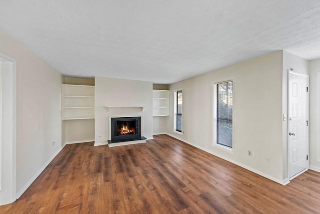 unfurnished living room featuring dark wood-style floors, a textured ceiling, a glass covered fireplace, and baseboards