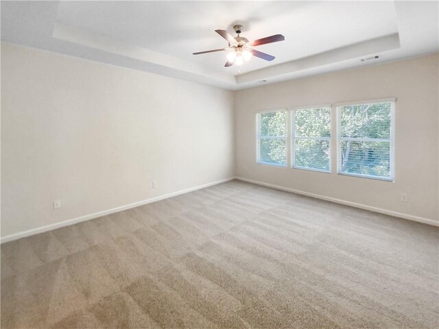 carpeted spare room featuring ceiling fan and a raised ceiling