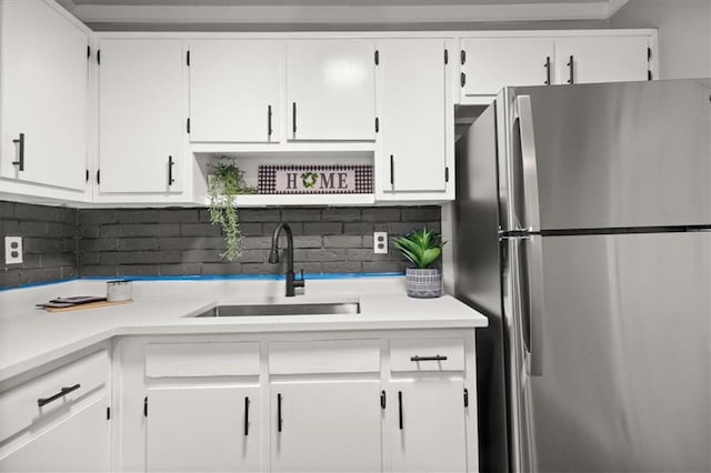 kitchen with decorative backsplash, white cabinetry, sink, and stainless steel refrigerator