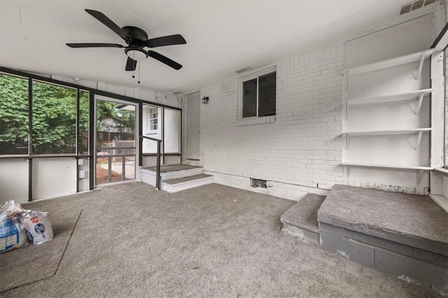 unfurnished living room with carpet flooring, ceiling fan, and brick wall