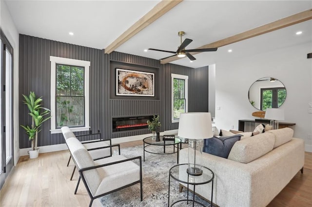 living room featuring ceiling fan, a fireplace, beamed ceiling, and a healthy amount of sunlight