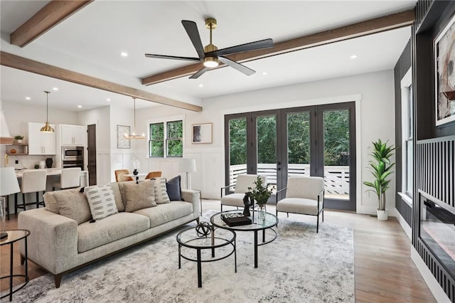 living room with ceiling fan with notable chandelier, beam ceiling, light wood-type flooring, and french doors