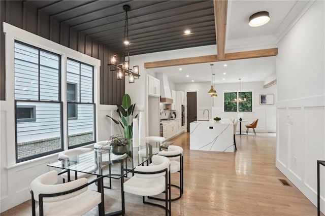 dining room with beam ceiling, light wood-type flooring, sink, and an inviting chandelier