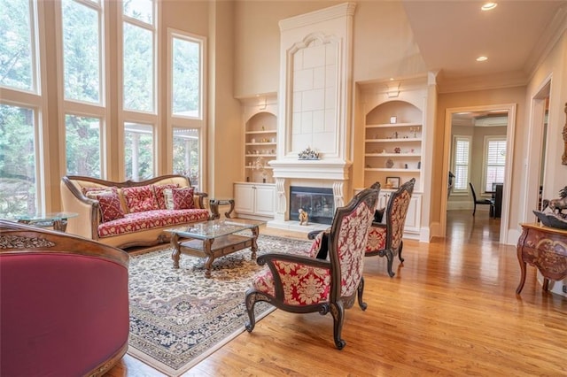 living room with a high ceiling, light wood-type flooring, built in features, and a wealth of natural light