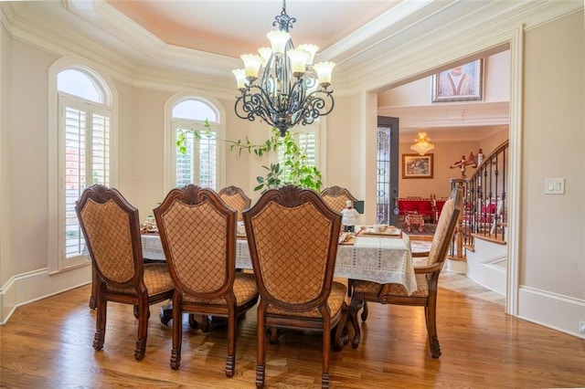 dining area featuring wood-type flooring, a tray ceiling, an inviting chandelier, and crown molding