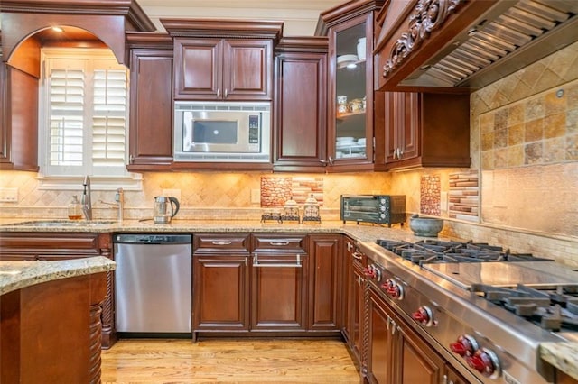 kitchen featuring custom exhaust hood, light wood-type flooring, decorative backsplash, and appliances with stainless steel finishes