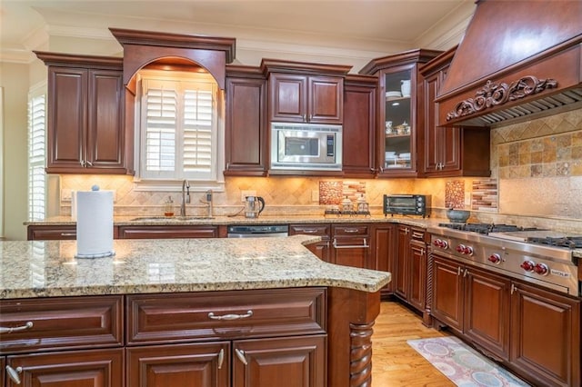 kitchen with custom exhaust hood, sink, light wood-type flooring, ornamental molding, and appliances with stainless steel finishes