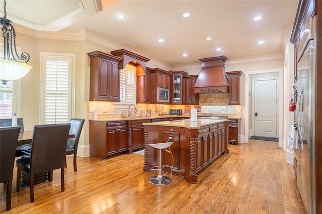 kitchen featuring light wood-type flooring, premium range hood, crown molding, a center island, and stainless steel microwave