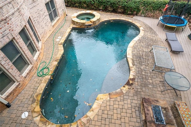 view of swimming pool with a trampoline and an in ground hot tub