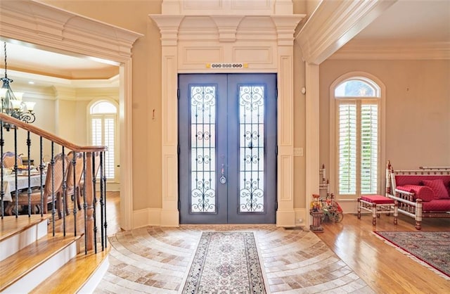 entryway with a healthy amount of sunlight, crown molding, light hardwood / wood-style flooring, and french doors