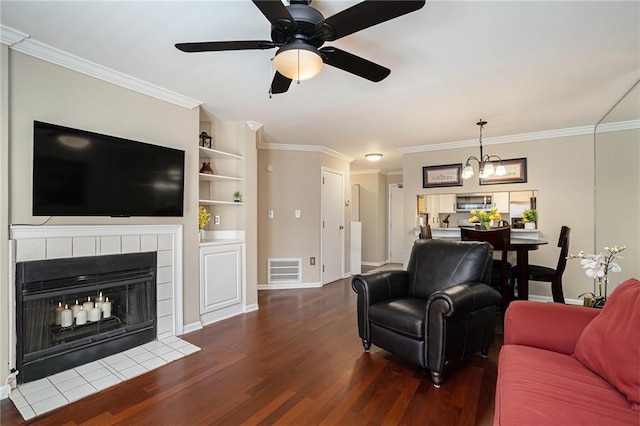 living room with dark wood-type flooring, ceiling fan with notable chandelier, ornamental molding, and a fireplace