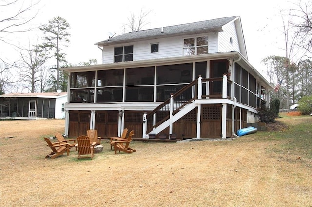 back of property featuring stairway, a sunroom, a lawn, and a fire pit