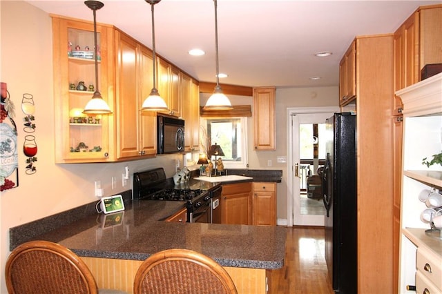 kitchen with dark countertops, a peninsula, black appliances, and wood finished floors