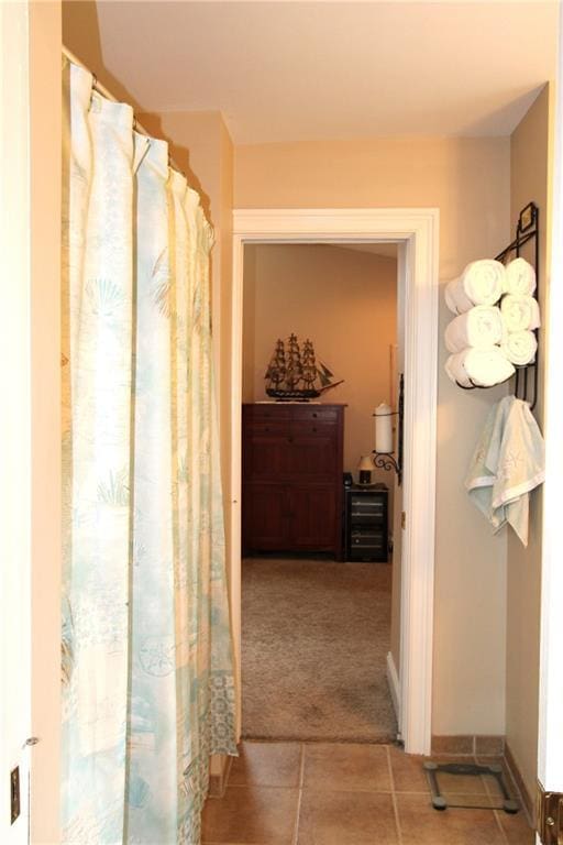 hallway with carpet floors, baseboards, and tile patterned floors