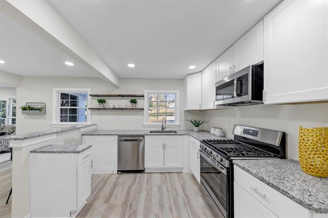 kitchen featuring light stone counters, stainless steel appliances, sink, light hardwood / wood-style flooring, and white cabinets