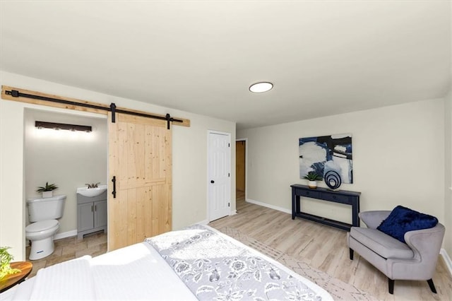 bedroom featuring sink, light hardwood / wood-style flooring, ensuite bath, a barn door, and a closet