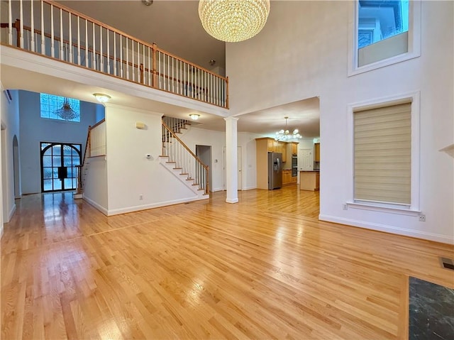 6765 Crofton Dr, Alpharetta, GA 30005 - unfurnished living room featuring a chandelier, a high ceiling, light wood-style flooring, baseboards, and stairway