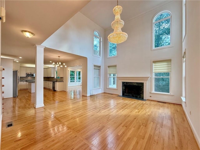 6765 Crofton Dr, Alpharetta, GA 30005 - unfurnished living room featuring a chandelier, a premium fireplace, light wood-style flooring, a towering ceiling, and baseboards